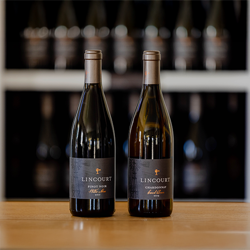 Two bottles of Lincourt wine on a wooden table with a blurred wine wall backdrop